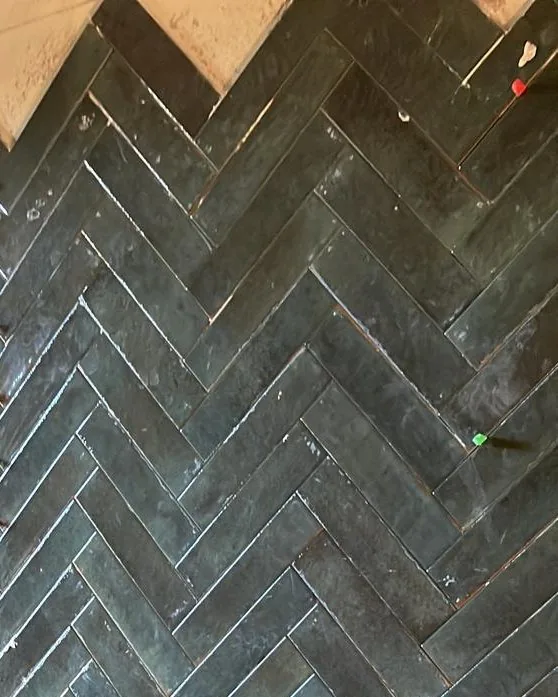 Parete rivestita a spina di pesce in piastrelle smaltate verdi, con il bordo superiore a zig zag