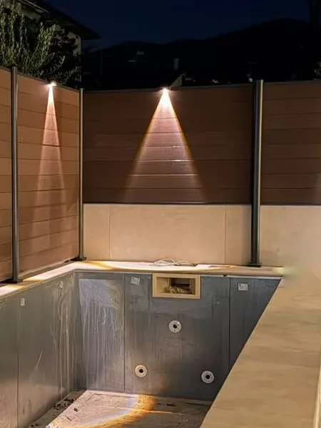 Vasca della piscina in fase di completamento con illuminazione serale sulla recinzione